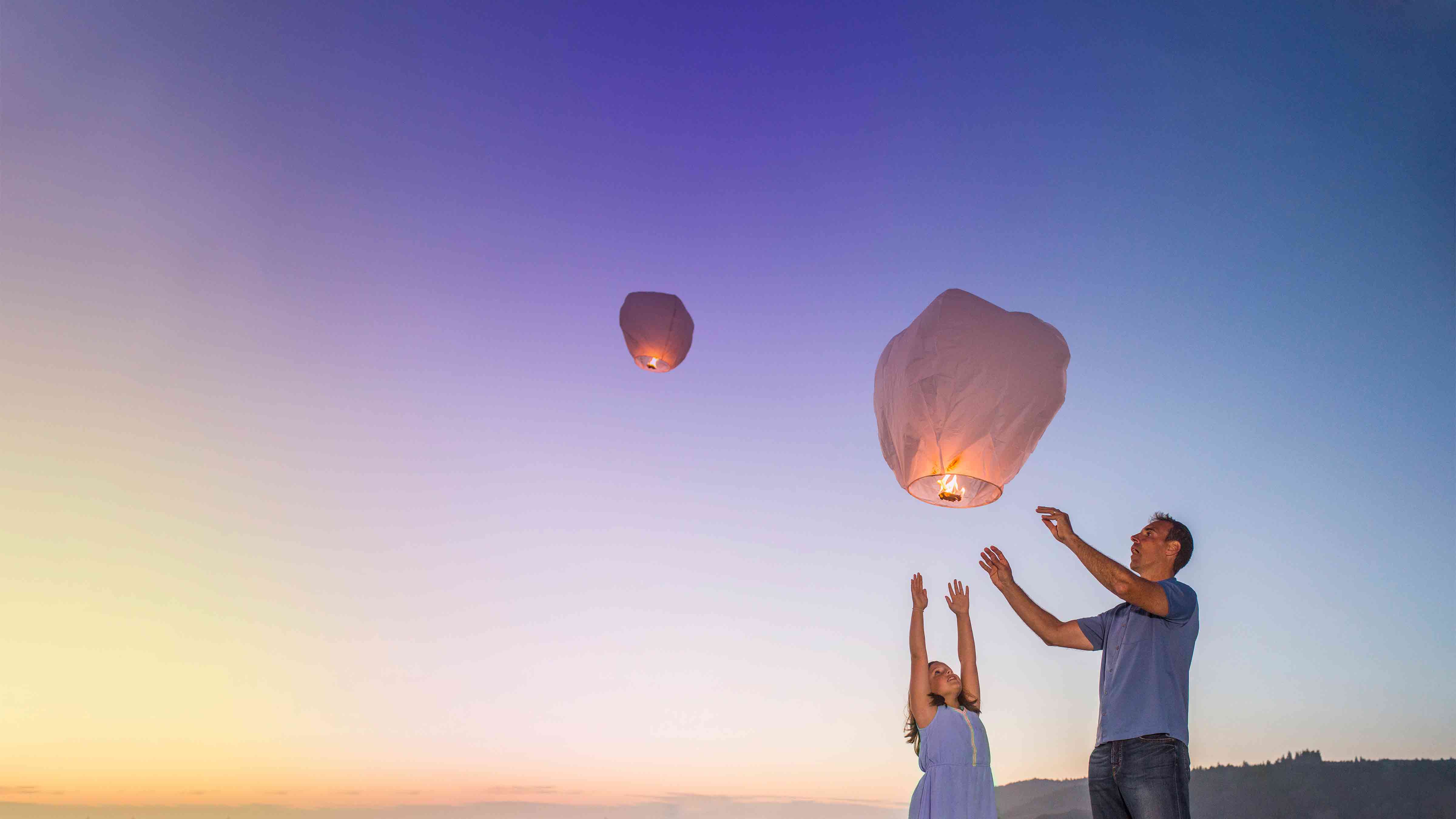 Father and daughter release white paper lanterns into the sky 